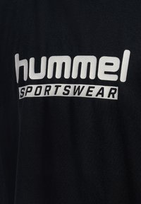 Schwarzer Stoff mit weißem "hummel SPORTSWEAR"-Text bedruckt.