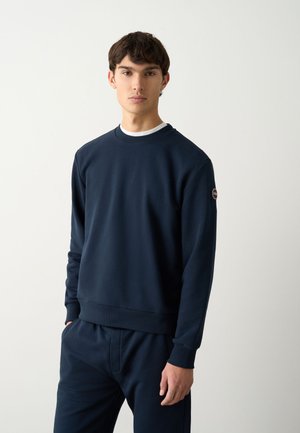 Navy blue sweatshirt made of soft fabric, featuring a crew neckline and ribbed cuffs, displayed on a model with matching pants.