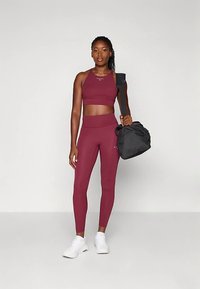 Haut court de sport marron foncé et leggings assortis en matière extensible, associés à des baskets blanches et un sac de sport noir.