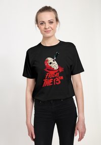 Camiseta negra de algodón con un gráfico de una máscara de hockey, un cuchillo y manchas de sangre, junto con el texto "VIERNES 13" en rojo.