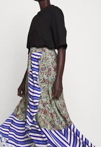 Černý krátký rukáv top spárovaný s dlouhou sukní s zeleným paisley vzorem a modrými pruhovanými akcenty. Sukně má volánkový lem.