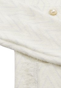 Sciarpa bianca intrecciata con un motivo a zigzag in fili argentati, con dettagli a frange e un accento decorativo di bottone perla.