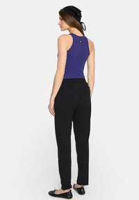 Fioletowy top na ramiączkach zestawiony z czarnymi, luźnymi spodniami. Strój ma swobodny krój, gładką teksturę i minimalistyczne akcenty.