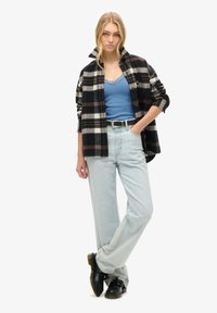 Zwart-wit geruite flanellen blouse over een blauwe tanktop, gecombineerd met lichtblauwe wijde jeans en zwarte schoenen, met een zilveren riem.