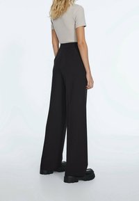 Black wide-leg trousers with a high waist, made from a smooth fabric. Details include a tailored look and large side pockets.