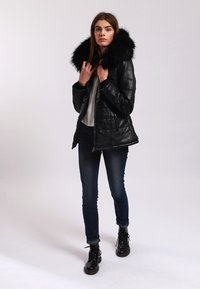 Svart läderjacka med en stor fuskpälskrage, dragkedjestängning, vadderad design, parat med mörka jeans och svarta kängor.