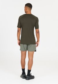 Olivgrünes sportliches T-Shirt mit kurzen Ärmeln, strukturiertem Stoff und Schulternähten. Kombiniert mit hellgrünen Shorts und schwarzem Schuhwerk.