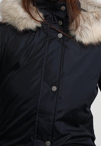 Marineblauwe pufferjack met een faux fur kraag, voorzien van drukknoopsluitingen en een gladde, doorgestikte textuur op het lijf.