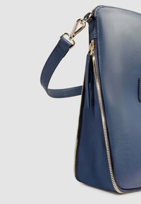 Sac en cuir marine avec une finition texturée, présentant des accessoires en métal doré et une ouverture zippée. Inclut une bandoulière amovible pour plus de polyvalence.