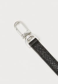 Bracelet en cuir noir avec un motif texturé et un fermoir en métal argenté pour une fixation sécurisée. Vue en gros plan mettant en évidence les détails du matériel.