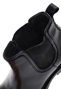 Stivaletto Chelsea in pelle nera con pannelli elastici laterali e linguetta sul tallone, angolato per mostrare la parte superiore aperta e i dettagli delle cuciture.