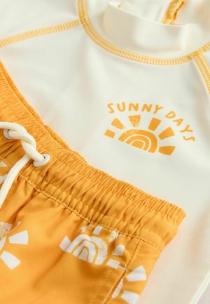 Fehér rash guard narancssárga varrással, "SUNNY DAYS" felirattal. Sárga fürdőnadrág fehér nap- és szivárványmintákkal.