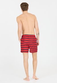 Shorts de bain rayés rouge et marine avec une taille élastique et une poche latérale, fabriqués en tissu léger. Conçus pour une utilisation décontractée à la plage.
