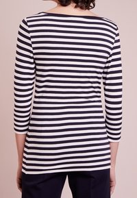 Raidallinen pitkähihainen toppi valkoisena ja laivastonsinisenä, pyöreällä kaula-aukolla ja istuvalla siluetilla, valmistettu sileästä, kevyestä kankaasta.