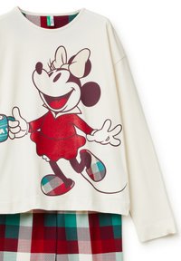 Top de manga larga color crema con un gráfico de un personaje de dibujos animados vestido de rojo, con pantalones de cuadros en rojo, verde y azul debajo.