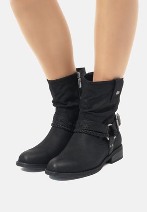 Botines negros con parte superior de tela arrugada, detalle de tira trenzada, acentos metálicos y un tacón bajo. Cierre lateral para un uso fácil.