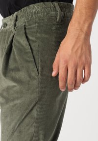 Pantalons en velours côtelé khaki avec des côtes verticales, taille élastique, poches latérales et une coupe décontractée. Le tissu a une texture douce.