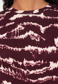 Bordo majica s teksturiranim, valovitim krem uzorkom, okruglim izrezom i suptilnim detaljima šavova, izrađena od mekog, rastezljivog materijala.