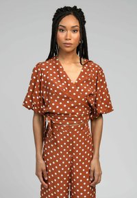 Haut croisé à pois marron avec des manches ballons courtes et un pantalon taille haute assorti, présentant un décolleté en V et un détail à nouer à la taille.