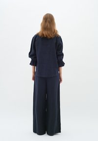 Camicia in lino blu navy con maniche a sbuffo e polsini elasticizzati, abbinata a pantaloni larghi blu navy. Design minimalista, mostrata di schiena.