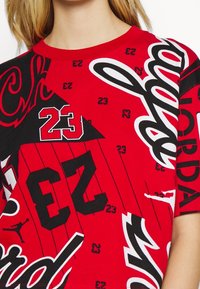 Czerwona bawełniana koszulka z grafikami, w tym "Jordan", numerem 23 i sylwetkami. Czarno-białe akcenty kontrastują z czerwonym tłem.