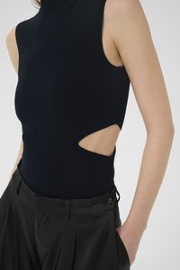 Marinefarbene ärmellose Bluse mit einer taillierten Silhouette, ausgestattet mit einem Stehkragen und einem Ausschnitt an der Seite, kombiniert mit hochgeschnittenen schwarzen Hosen.