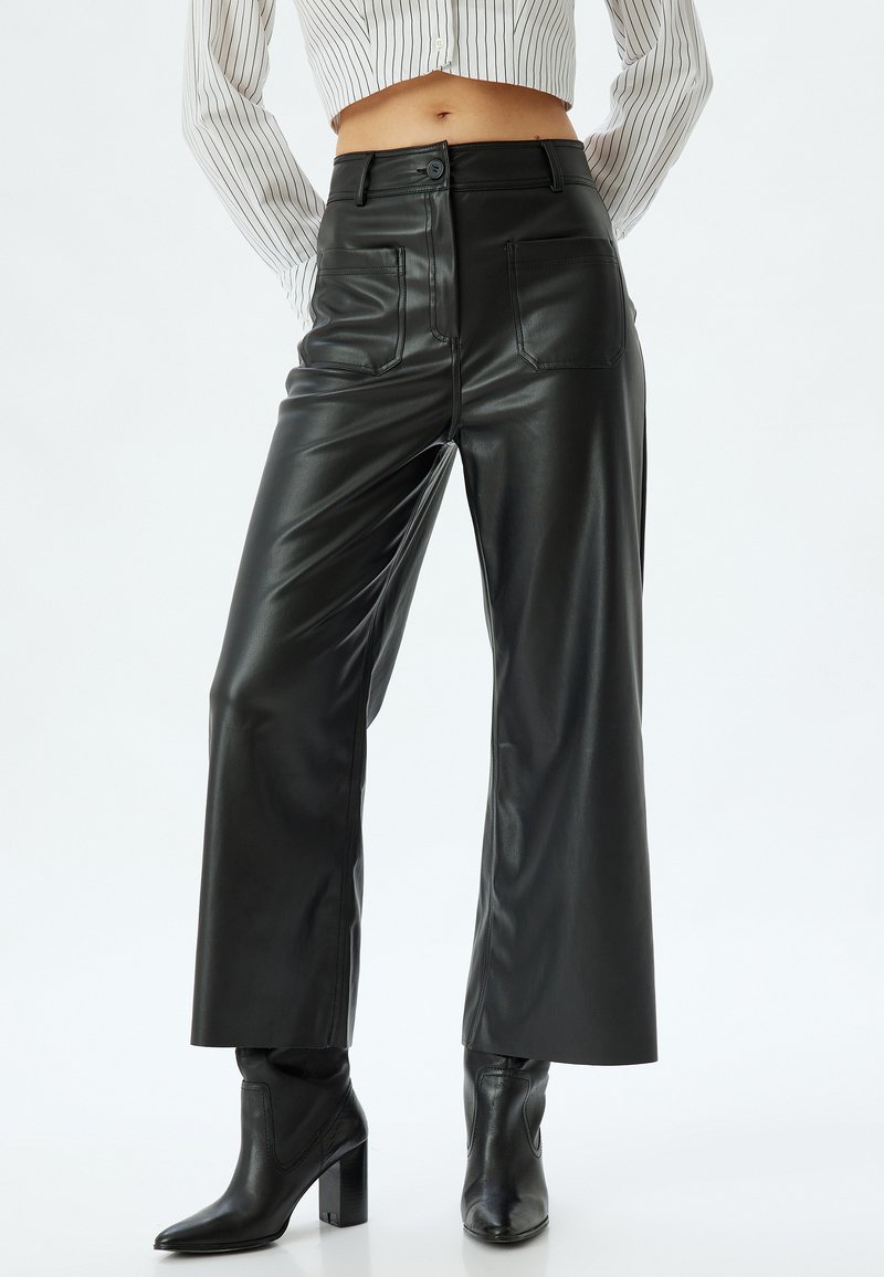 Zwarte nepleren wijde broek met zakken, een gladde textuur, hoge taille en een knoopsluiting, gecombineerd met zwarte hoge enkelboots.