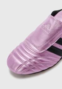 Sapatilha Adidas metálica rosa com costura texturizada e riscas pretas em fundo branco, mostrando os detalhes da frente e lateral.