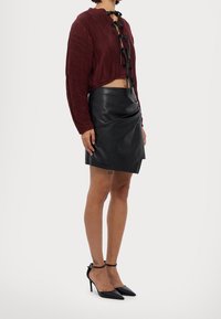 Top corto in corduroy bordeaux con fiocco nero, abbinato a una mini gonna in pelle nera, completato da tacchi a spillo neri.