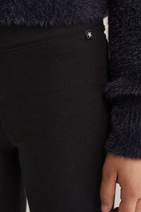 Fekete leggings sima anyagból, rugalmas derékpánttal és egy kis csillaglogó címkével a deréknál. Látható textúrájú tengerészkék pulóver.