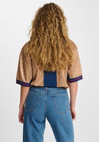 Kortærmet cykeltrøje i et lysebrunt tekstureret mønster med en ensfarvet navyblå bagpanel. Har røde og blå striber på ærmerne.