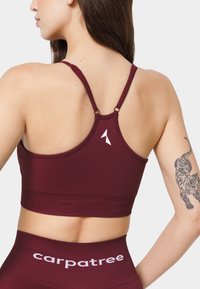 Burgundijas sporta krūšturis ar racerback dizainu, gludu tekstūru un balto logo detaļu. Pāris ar saskaņotām augstām leggām.