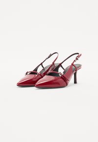 Des escarpins à bride arrière en cuir verni rouge présentent des bouts pointus, des bretelles étroites et un petit talon carré avec un éclat subtil.