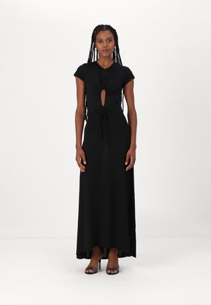 Abito maxi nero con dettaglio a nodo sul décolleté, maniche corte e accentuazione cut-out. Tessuto liscio con una leggera lucentezza, indossato con tacchi neri.