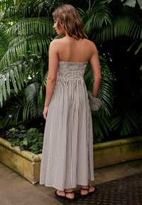 Trägerloses Maxikleid mit gerafftem Oberteil aus gestreiftem Stoff; verfügt über einen fließenden Rock und wird mit schwarzen flachen Sandalen und einer gemusterten Clutch kombiniert.