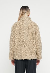 Giacca fluffy beige con colletto alto, superficie testurizzata e vestibilità comoda; mostrata da dietro con maniche a taglio dritto e senza chiusure.