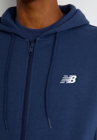 Sweatshirt navy com fecho éclair e capuz com cordão, em material de mistura de algodão, apresentando um logotipo bordado branco no peito.