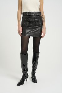 Black leather mini skirt with three wide belts, paired with opaque black tights and glossy knee-high boots. Smooth texture, fitted design.