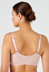 Sujeta con tirantes anchos y de un suave tejido en color rosa claro. Con bordes scallop y características de tirantes ajustables y cierre de gancho y ojo en la parte trasera.
