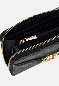 Billetera negra texturizada con cremallera dorada, bolsillo interior con cremallera para monedas, ranuras para tarjetas y un broche decorativo dorado en la parte frontal.