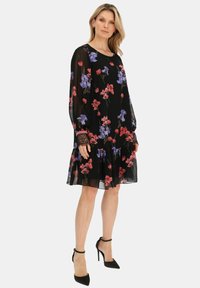 Kwiatowa sukienka z szyfonu na czarnym tle, z czerwonymi i fioletowymi kwiatami, długimi rękawami, koronkowymi mankietami oraz falbaną na dole.