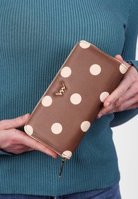 Brown wallet with large cream polka dots, gold hardware, and zip closure. Made from smooth leather with a rectangular shape.