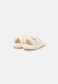 Cream-colored faux fur slippers with open toe, a soft texture, and a decorative buckle accent. Textured rubber sole for grip.