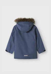 Blå vandtæt parka med pelsforet hætte, lange ærmer og lige snit. Har sorte detaljer ved manchetten og et logo-mærke i bunden.