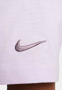 Tela morada clara de Nike con un pequeño logo de swoosh bordado en gris oscuro. El material es suave y tiene una textura sutil.