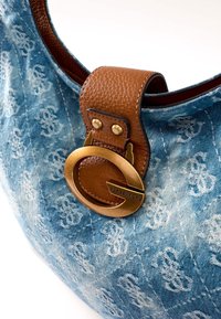 Sac Guess en denim bleu avec motif logo répétitif, bandoulière en cuir marron et boucle circulaire dorée avec logo Guess.