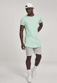 Mintgrøn crew-neck T-shirt med korte ærmer, kombineret med grå denimshorts og hvide sneakers, afsluttet med en hvid kasket.