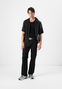 Black short-sleeve shirt and black t-shirt paired with black trousers. The outfit features a silver buckle belt and black and white sneakers.