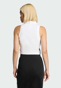 Biały krótki top bez rękawów z wysokim kołnierzem, zestawiony z czarną prążkowaną spódnicą. Top ma dopasowany fason i gładką fakturę.