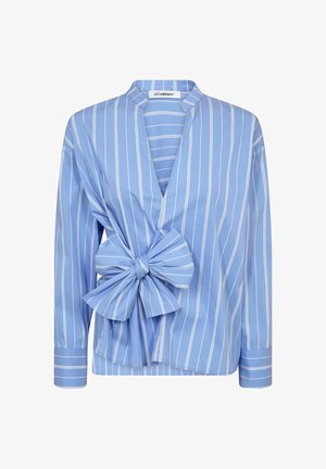 Sinipunaiset raidoitetut pusero, jossa on V-pääntie, suuri solki yksityiskohtana sivussa, pitkät hihat ja pehmeä puuvillakangas.